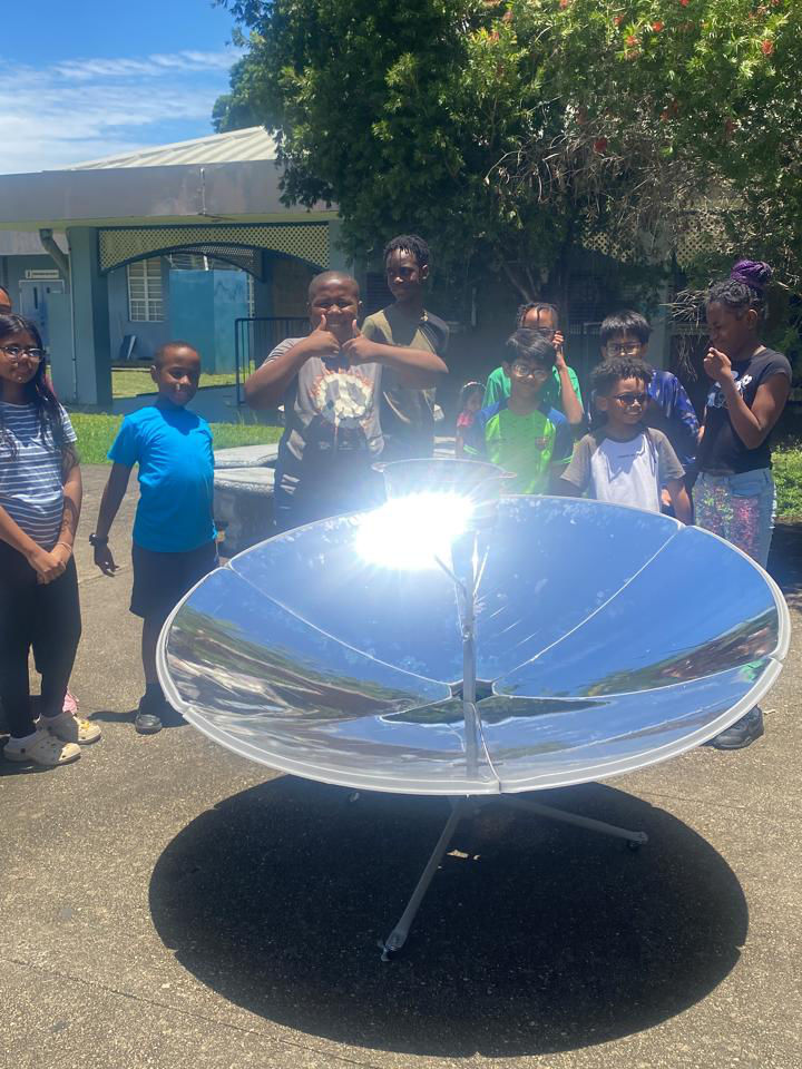 Children attending NGC Green's net zero camp stand around a solar dish